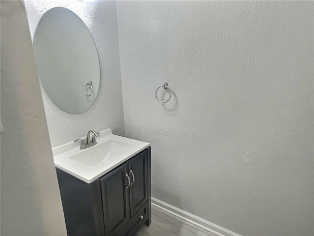 bathroom featuring a textured wall, baseboards, wood finished floors, and vanity