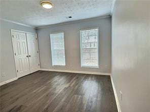 spare room featuring baseboards, a textured ceiling, ornamental molding, and wood finished floors