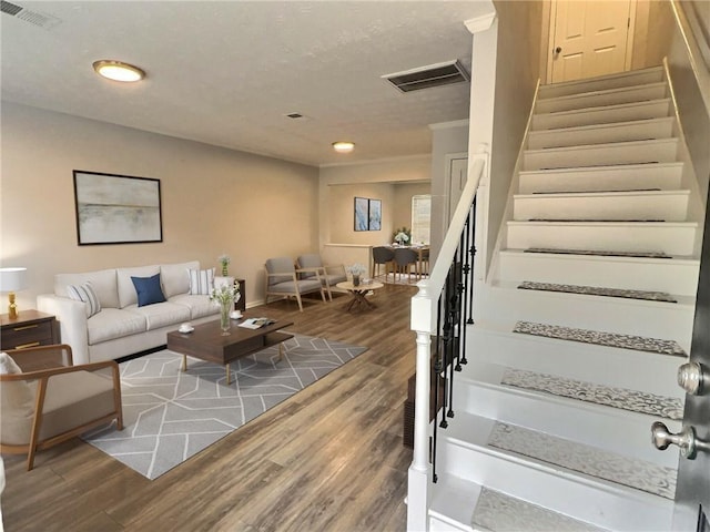 living room featuring stairs, visible vents, and wood finished floors