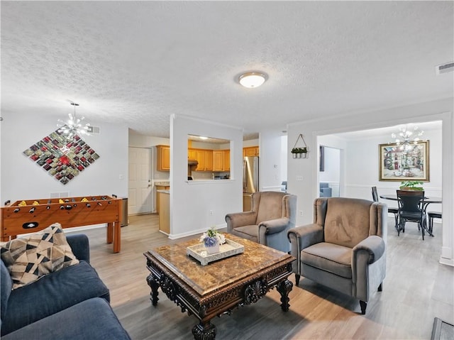 living area featuring a chandelier, a textured ceiling, visible vents, and light wood-style floors