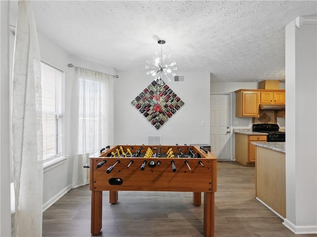 rec room featuring a textured ceiling, light wood finished floors, visible vents, and an inviting chandelier