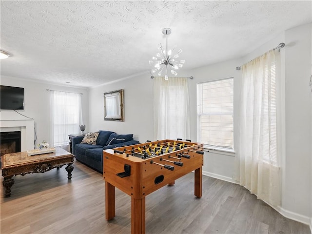 rec room with a textured ceiling, a fireplace, wood finished floors, and an inviting chandelier