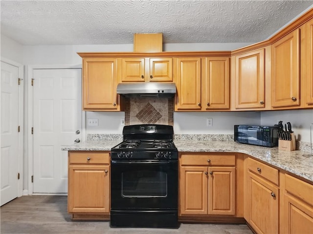 kitchen featuring light stone counters, wood finished floors, under cabinet range hood, a textured ceiling, and black appliances