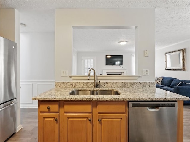 kitchen featuring stainless steel appliances, open floor plan, a sink, and light stone countertops