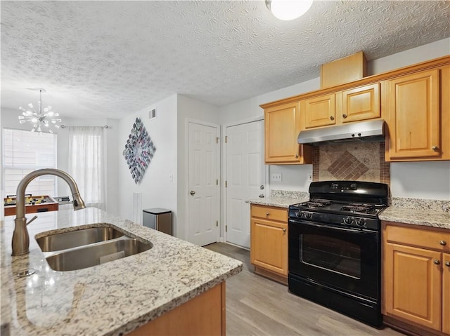 kitchen featuring light stone counters, light wood-style flooring, under cabinet range hood, a sink, and black gas stove