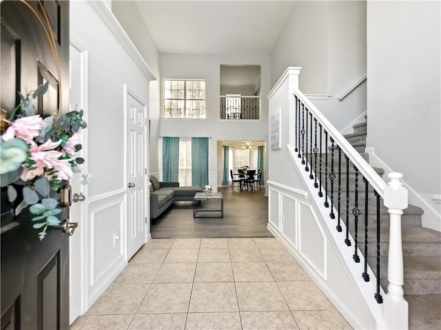 entryway featuring stairs, a decorative wall, a towering ceiling, and light tile patterned floors