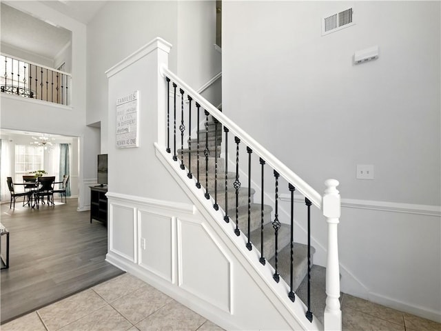 stairs with a wainscoted wall, tile patterned flooring, visible vents, and a decorative wall