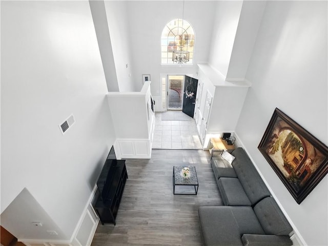 living room featuring a towering ceiling, visible vents, a chandelier, and wood finished floors