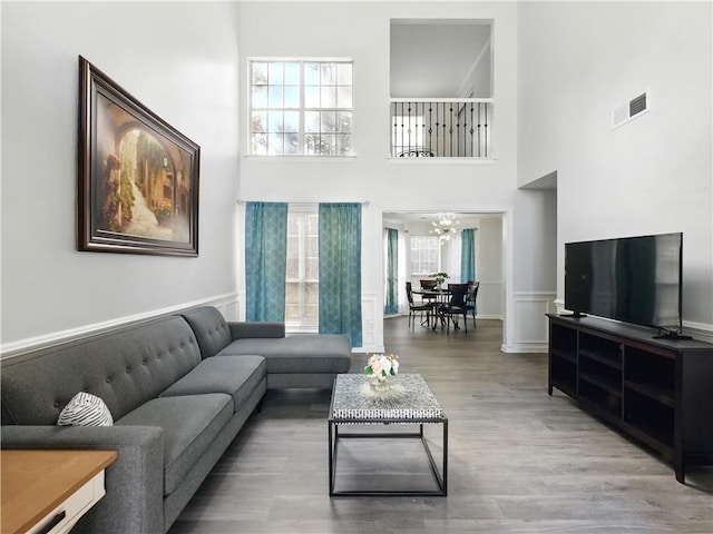 living area featuring a towering ceiling, an inviting chandelier, visible vents, and wood finished floors