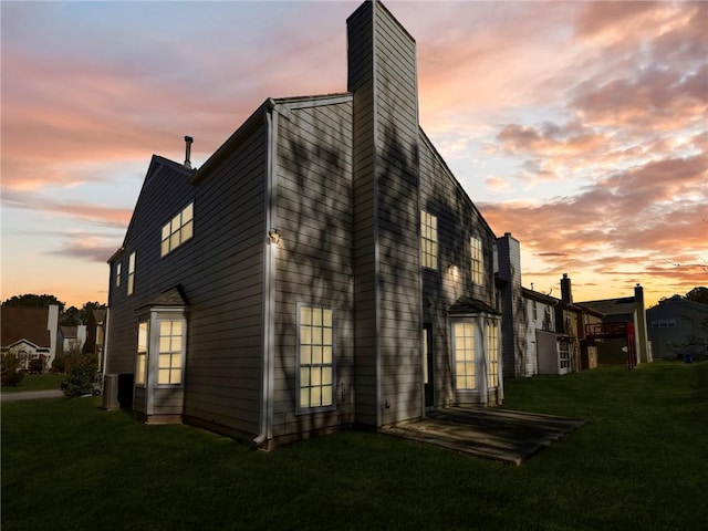 property exterior at dusk with a lawn and a chimney