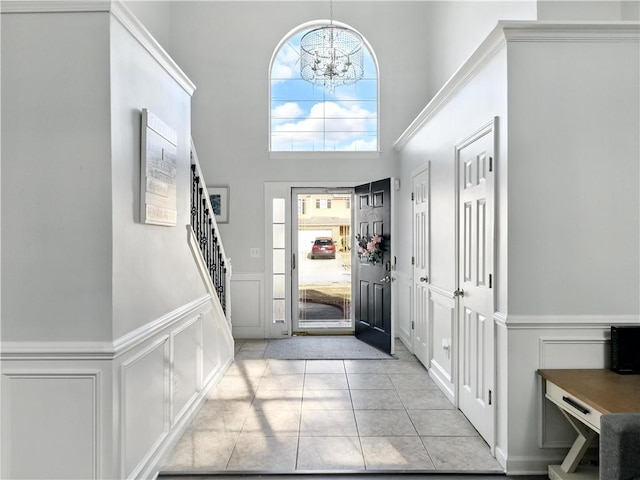 entryway featuring light tile patterned floors, a towering ceiling, stairway, a chandelier, and a decorative wall