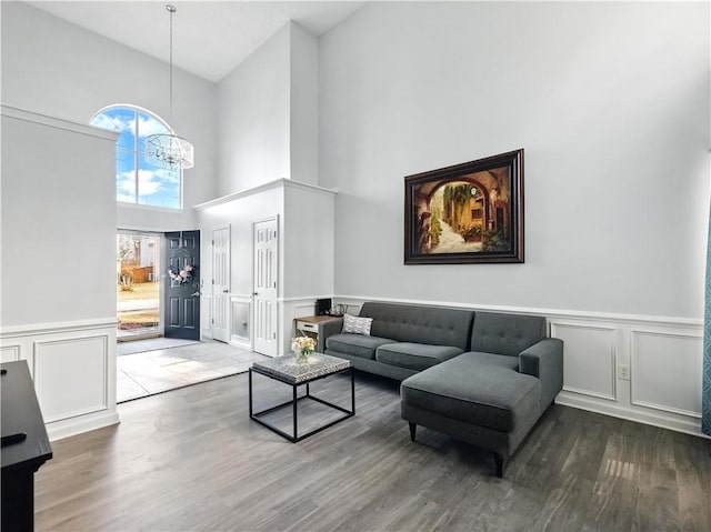 living area featuring a chandelier, high vaulted ceiling, wood finished floors, and a decorative wall