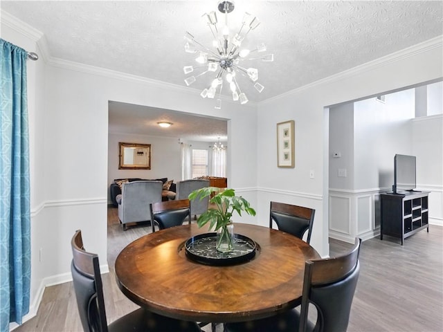 dining area featuring light wood finished floors, crown molding, a textured ceiling, and a notable chandelier