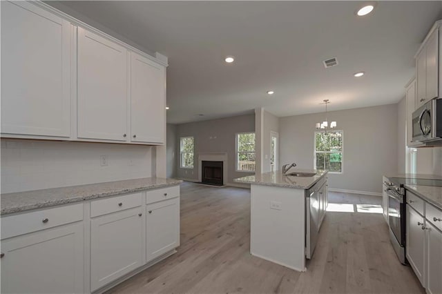 kitchen featuring backsplash, white cabinets, an island with sink, and appliances with stainless steel finishes