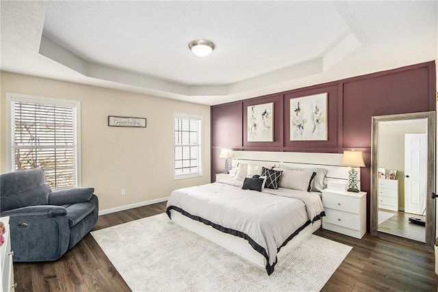 bedroom featuring a raised ceiling, baseboards, dark wood-type flooring, and multiple windows