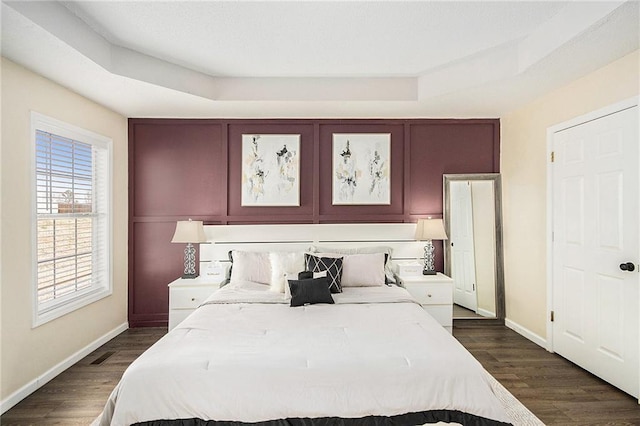 bedroom featuring baseboards, dark wood finished floors, and a tray ceiling