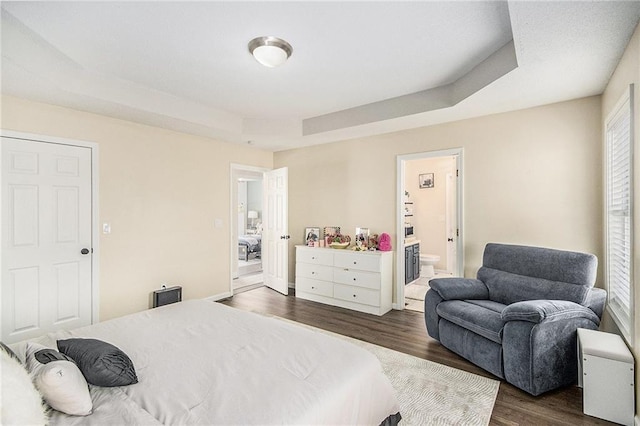 bedroom with a tray ceiling, connected bathroom, baseboards, and dark wood finished floors