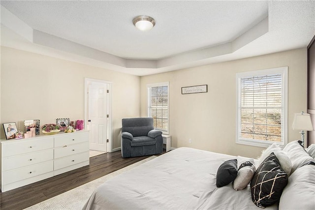 bedroom with a tray ceiling and dark wood-style floors