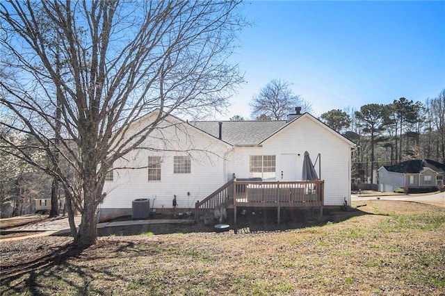rear view of property featuring central air condition unit, a wooden deck, a chimney, and a lawn