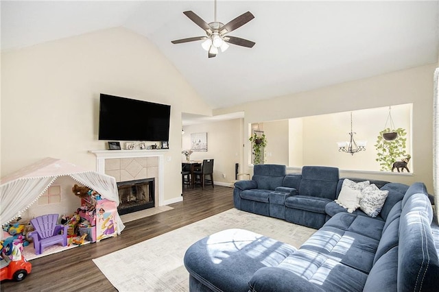 living area featuring wood finished floors, ceiling fan with notable chandelier, high vaulted ceiling, a tiled fireplace, and baseboards
