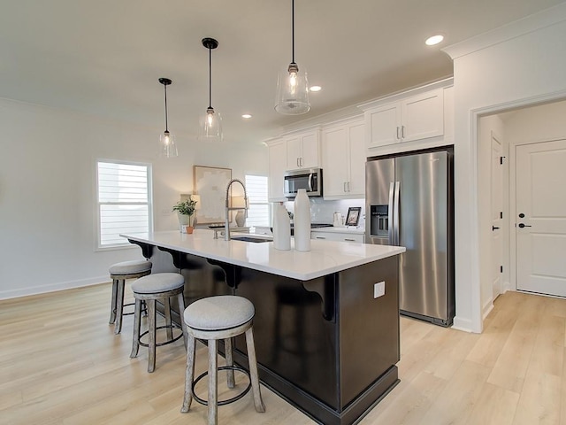 kitchen with sink, appliances with stainless steel finishes, a kitchen island with sink, hanging light fixtures, and white cabinets