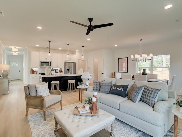 living room with ceiling fan with notable chandelier and light wood-type flooring