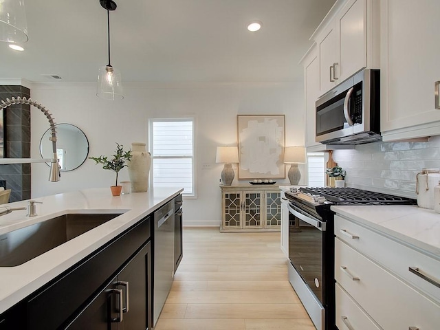 kitchen featuring appliances with stainless steel finishes, white cabinetry, tasteful backsplash, light hardwood / wood-style floors, and decorative light fixtures