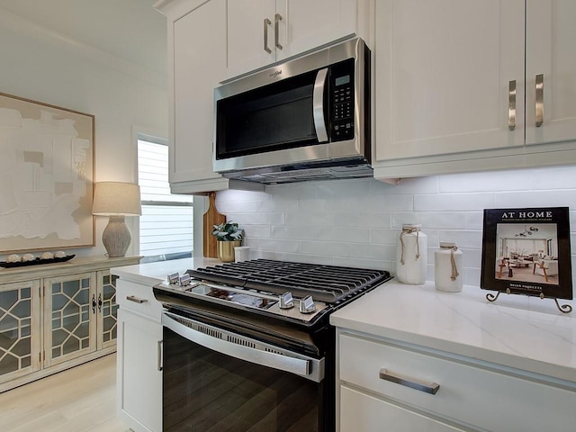 kitchen with white cabinetry, stainless steel appliances, light stone counters, and tasteful backsplash