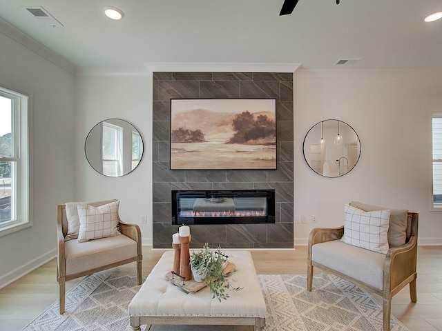 sitting room with crown molding, ceiling fan, a tile fireplace, and light wood-type flooring