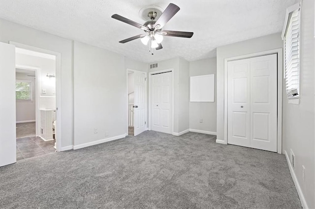 unfurnished bedroom featuring ensuite bath, light colored carpet, ceiling fan, multiple closets, and a textured ceiling