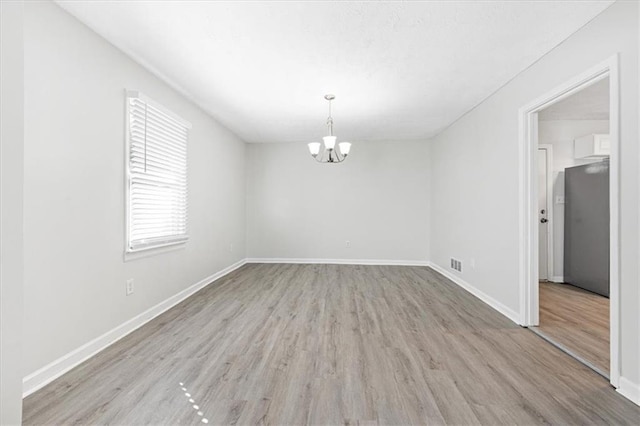 spare room with an inviting chandelier and light wood-type flooring