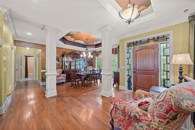 foyer with decorative columns, ornamental molding, wood-type flooring, a raised ceiling, and a chandelier