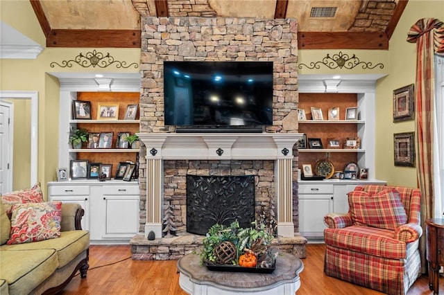 living area featuring visible vents, built in shelves, a stone fireplace, and wood finished floors