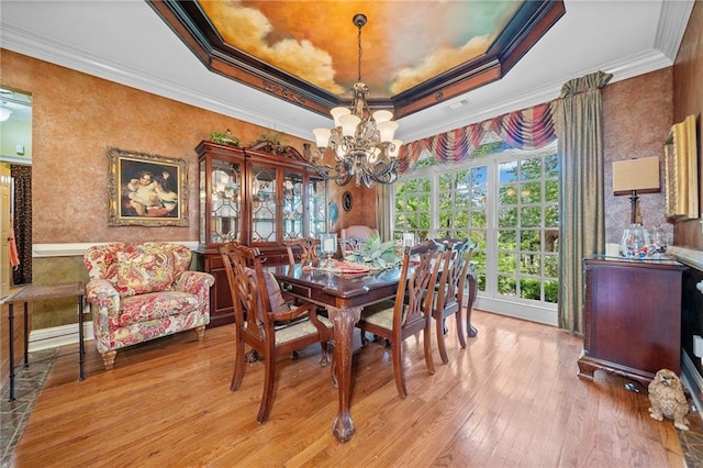 dining room with a tray ceiling, crown molding, a notable chandelier, and light wood-style floors