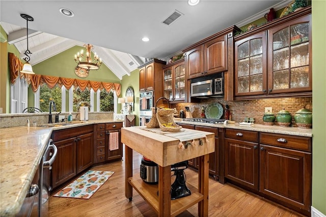 kitchen with a sink, appliances with stainless steel finishes, an inviting chandelier, lofted ceiling, and hanging light fixtures