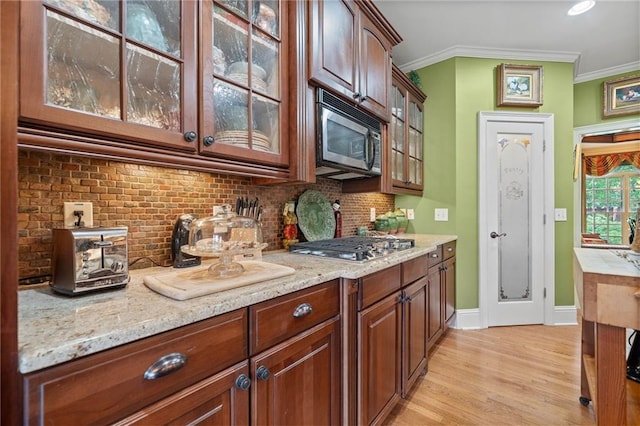 kitchen featuring tasteful backsplash, glass insert cabinets, crown molding, light stone countertops, and appliances with stainless steel finishes