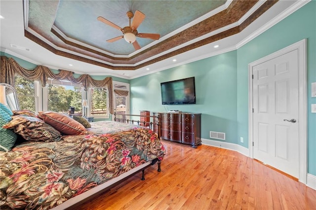 bedroom with a tray ceiling, visible vents, wood finished floors, and crown molding