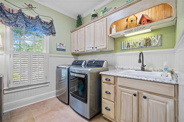 washroom with a wainscoted wall, washing machine and dryer, ornamental molding, cabinet space, and a sink