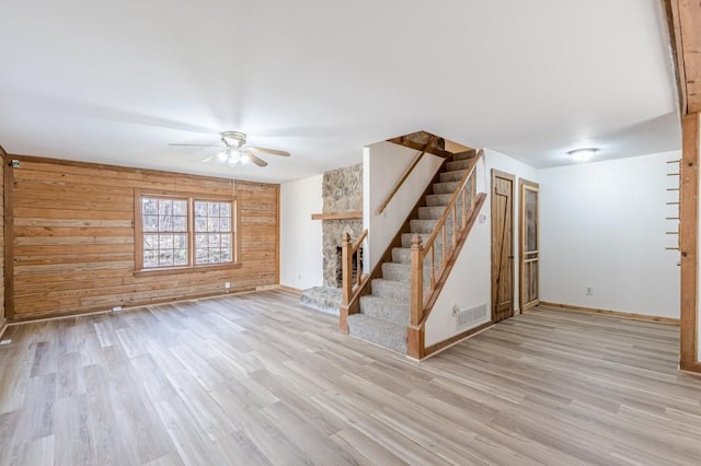 interior space featuring ceiling fan, wooden walls, light hardwood / wood-style floors, and a stone fireplace