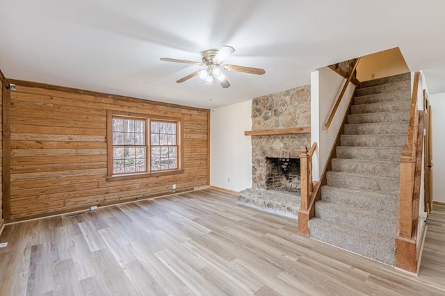 unfurnished living room with wooden walls, a fireplace, ceiling fan, and light hardwood / wood-style floors