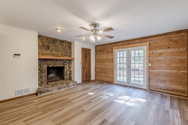 unfurnished living room with ceiling fan, wooden walls, and a stone fireplace