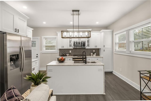 kitchen with appliances with stainless steel finishes, dark wood-type flooring, sink, decorative light fixtures, and a center island with sink