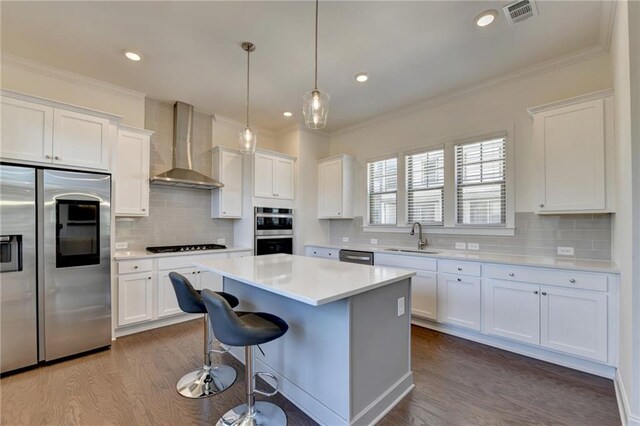 kitchen featuring stainless steel appliances, sink, wall chimney range hood, white cabinetry, and a kitchen island