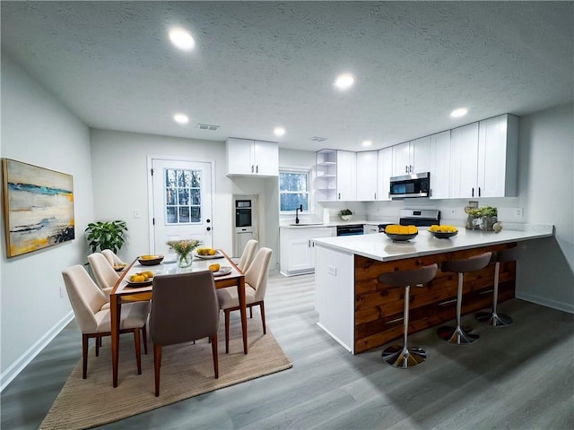 kitchen with white cabinetry, stainless steel appliances, light hardwood / wood-style flooring, kitchen peninsula, and a textured ceiling