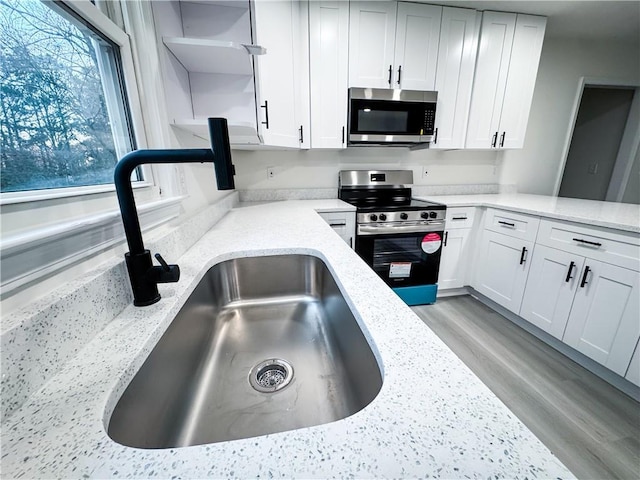 kitchen with sink, light stone countertops, appliances with stainless steel finishes, light hardwood / wood-style floors, and white cabinetry