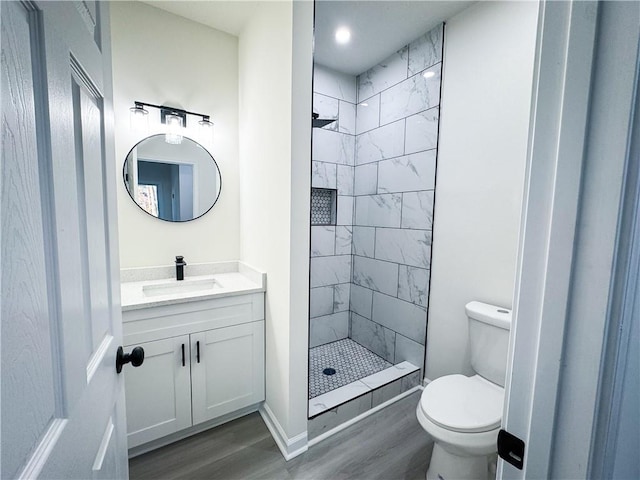 bathroom with tiled shower, wood-type flooring, vanity, and toilet