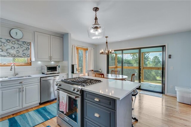 kitchen with sink, stainless steel appliances, a center island, a notable chandelier, and light wood-type flooring