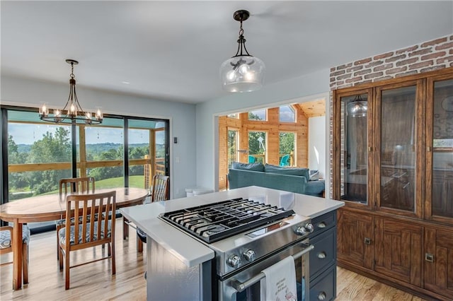 kitchen with stainless steel gas range oven, a chandelier, pendant lighting, light countertops, and light wood-style flooring