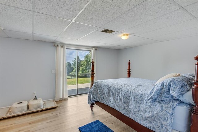 bedroom featuring access to outside, wood-type flooring, and a paneled ceiling