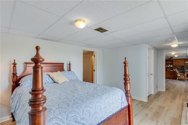 bedroom with light wood-type flooring and a drop ceiling